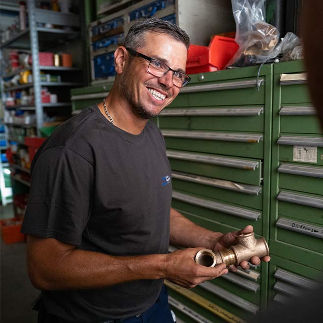 Robert Golombek in der Werkstatt der Firma Rolf Müller Haustechnik mit einer Messingarmatur in der Hand